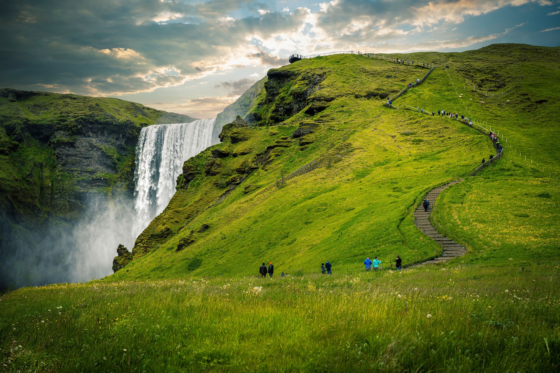 Tourists walking up path with waterfall and green grass in iceland